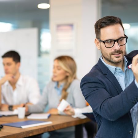 Focused businessman using whiteboard to write key points during a presentation, aiming to outline business plan for successful company growth to business partners.